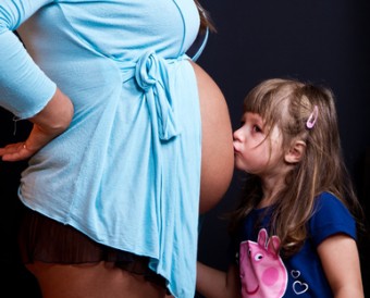 Child kissing belly of pregnant woman against black background