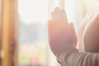 Hands of an unrecognizable woman standing by the window and praying